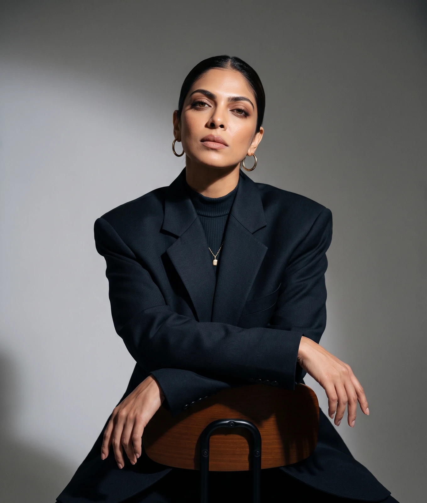 Nankii Siingh seated backwards on a chair in a black blazer, arms crossed over the backrest